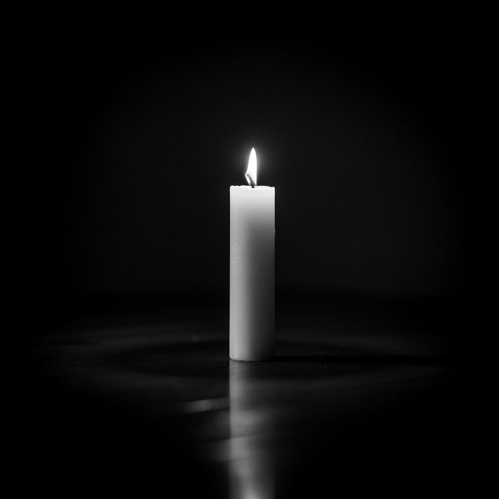 Minimalist black and white photo of a single white candle on a dark background, mourning, dignified.